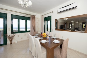 Uma sala de jantar com uma mesa de madeira posta para quatro pessoas, um candelabro e um espelho grande na parede.