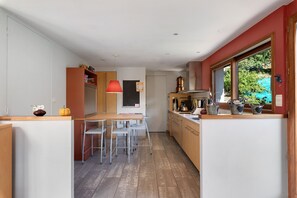 A modern kitchen with a dining area, featuring a central island, bar stools, and a red pendant light. - Villa 'Terre de Lumières' with View of Mount Néron in a Natural Setting (Quaix-en-Chartreuse)