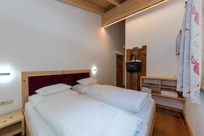A double bed with white linens, a wooden headboard, and a bedside table with a power outlet. - Chalets Glemmtal - Chalet Bergblick (Viehhofen)