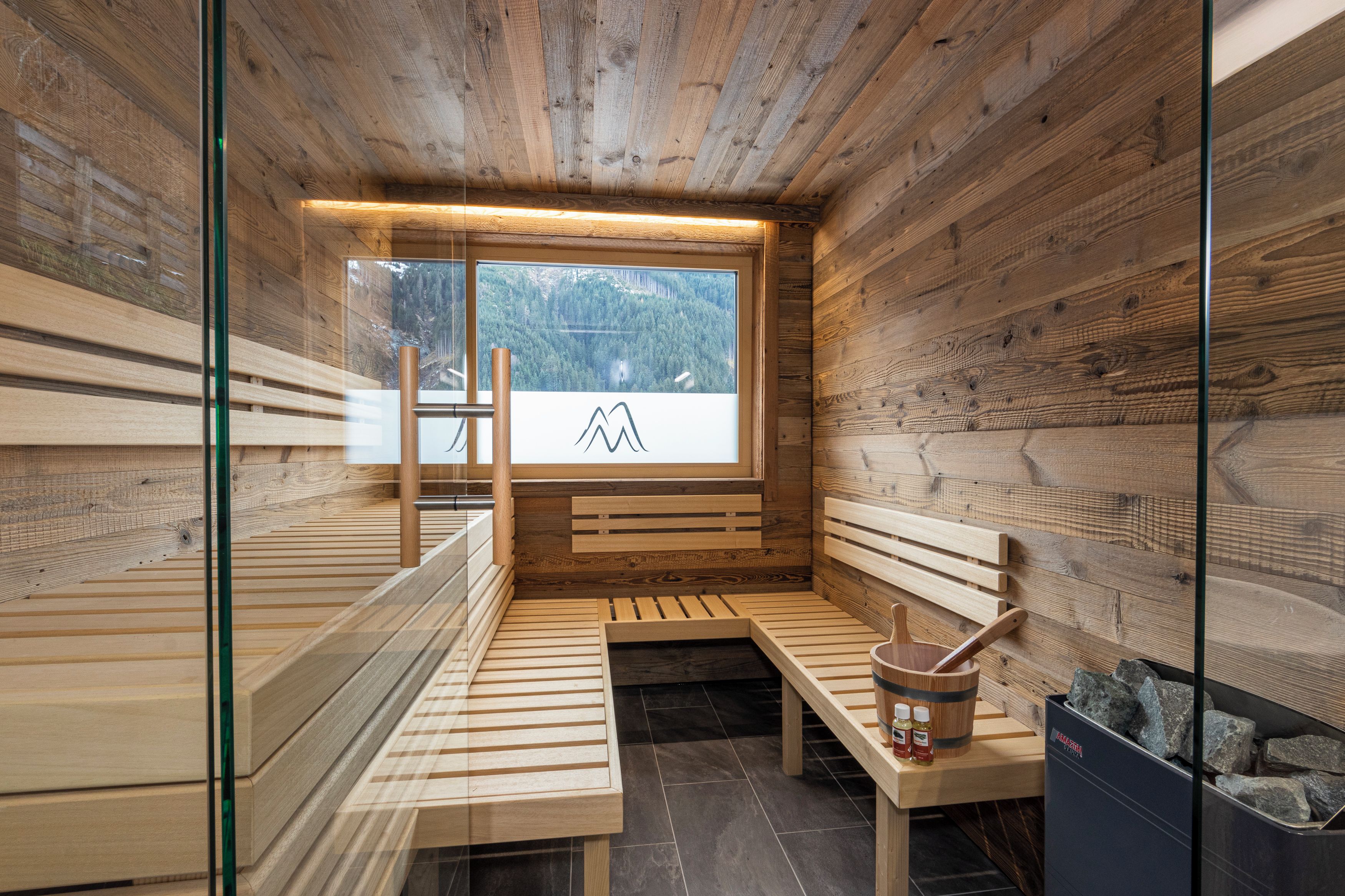 A sauna with wooden benches, a wooden bucket, and a stone-filled container.