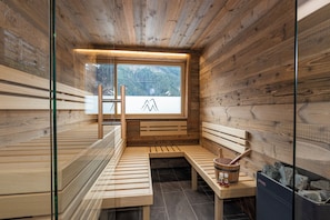 A sauna with wooden benches, a wooden bucket, and a stone-filled container. - Chalets Glemmtal - Chalet Bergblick (Viehhofen)