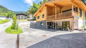 A wooden two-story building with a balcony, stone foundation, and potted plants in front. - Chalets Glemmtal - Chalet Bergblick (Viehhofen)