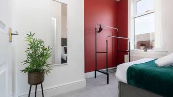 A bedroom with a bed, a window, a radiator, a mirror, and a plant.