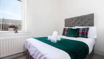 Ein ordentlich bezogenes Bett mit einer grünen Decke, einem weißen Kopfkissen und einem Karokissen.