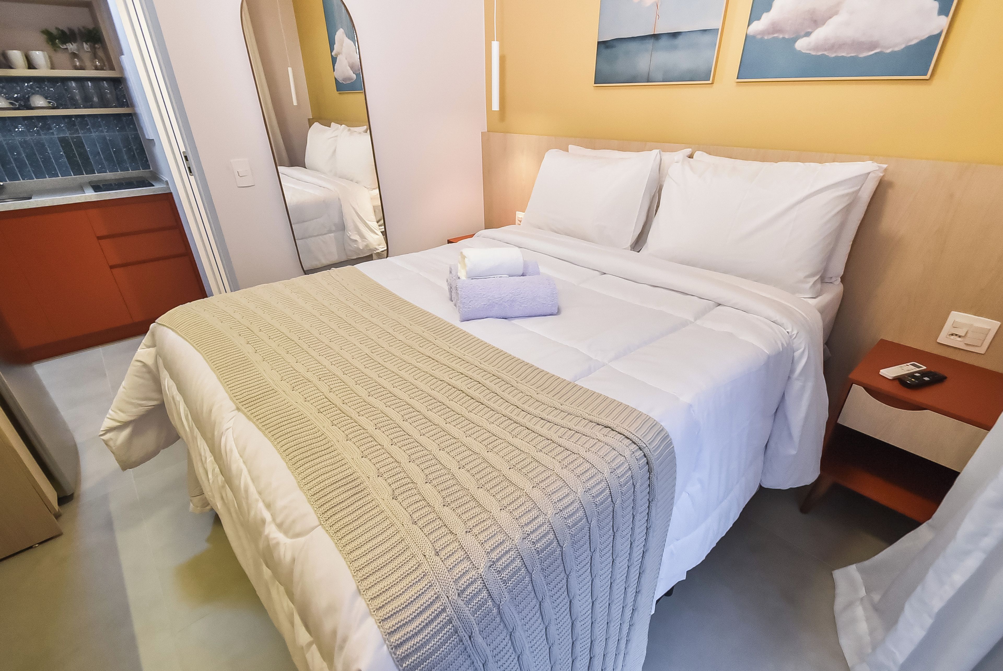 A hotel room with a bed, a bedside table, a nightstand, a wardrobe, and a mirror.
