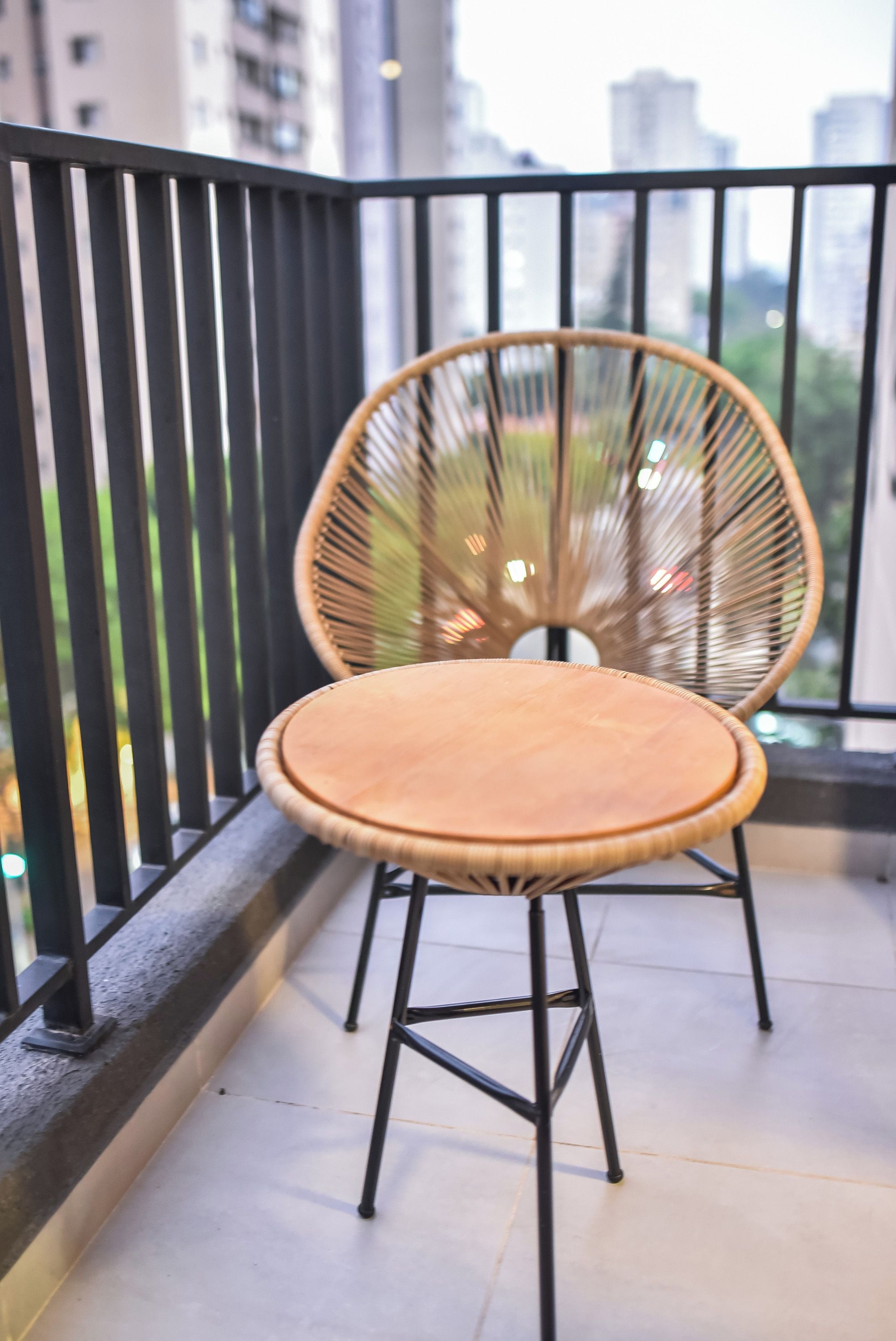 A wicker chair with a round seat and metal legs on a balcony with a black railing.