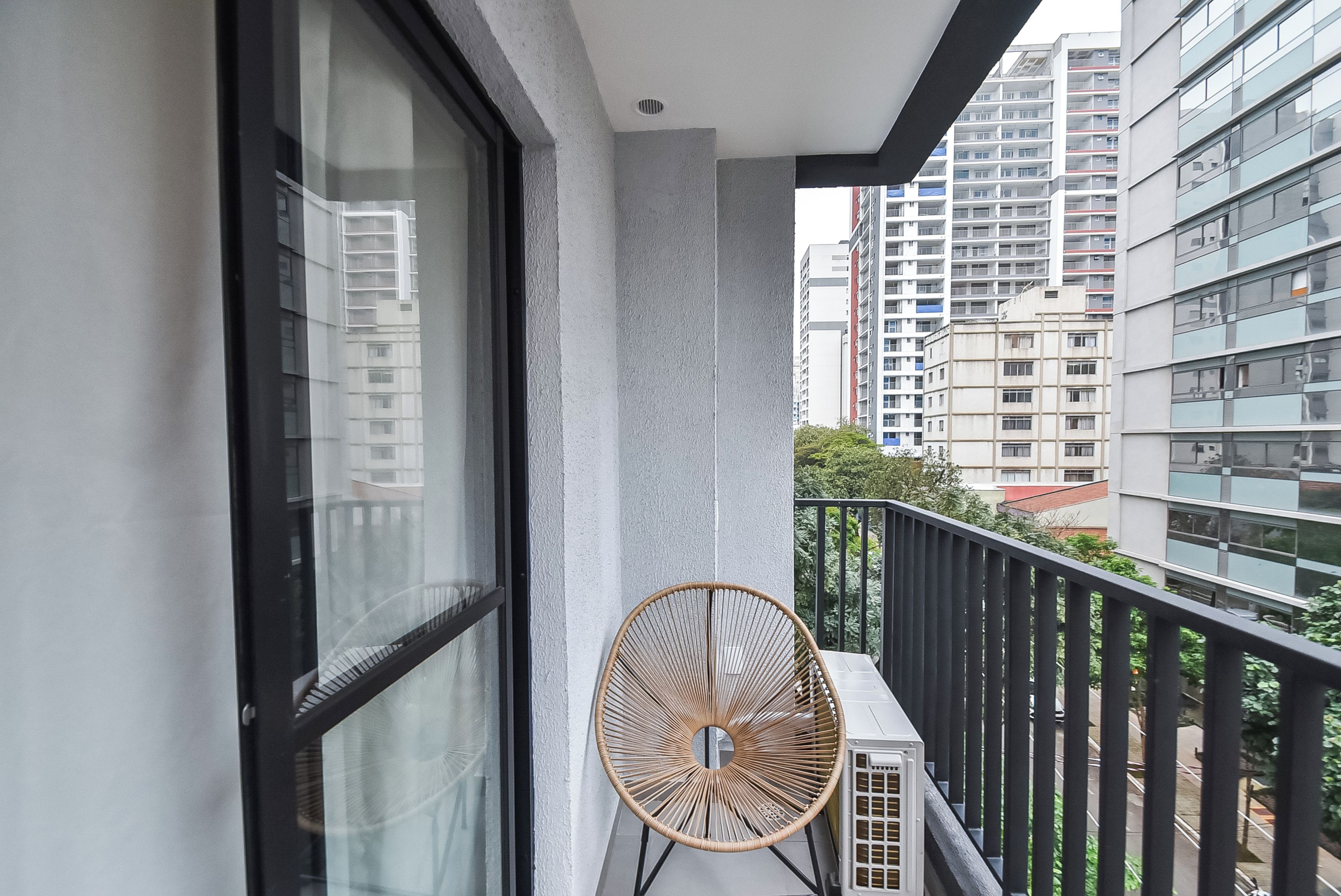 A balcony with a wicker chair, a window, and a view of high-rise buildings.