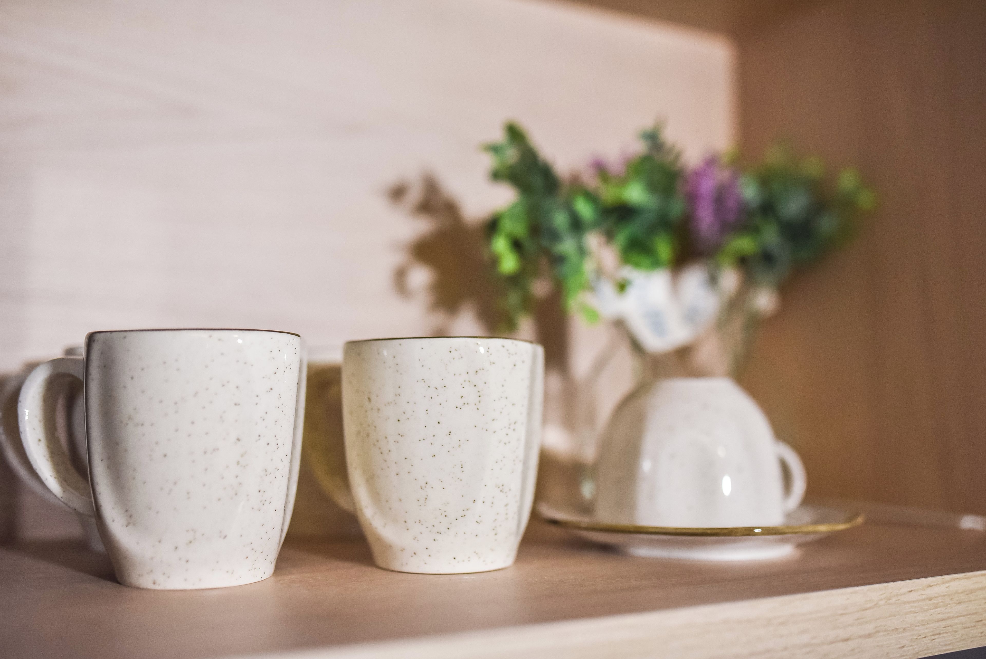 Two white ceramic mugs with speckles on a wooden surface.