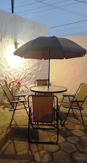 An outdoor patio with a round table and four chairs, an umbrella, and a potted plant. - Casa Amigos do Arraial (Arraial d'Ajuda)