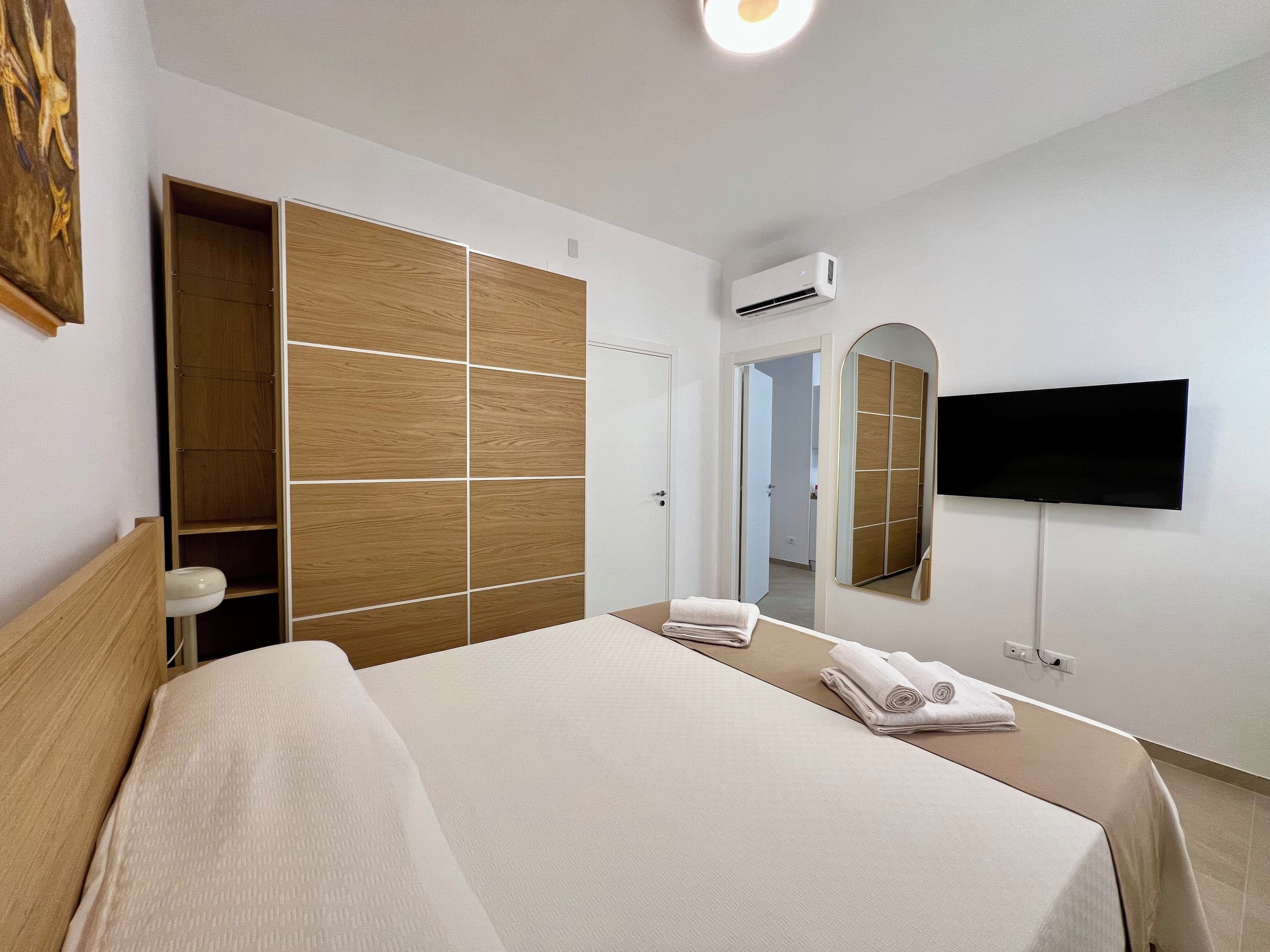 Quarto de hotel com cama, guarda-roupa, ar condicionado, televisão e espelho.