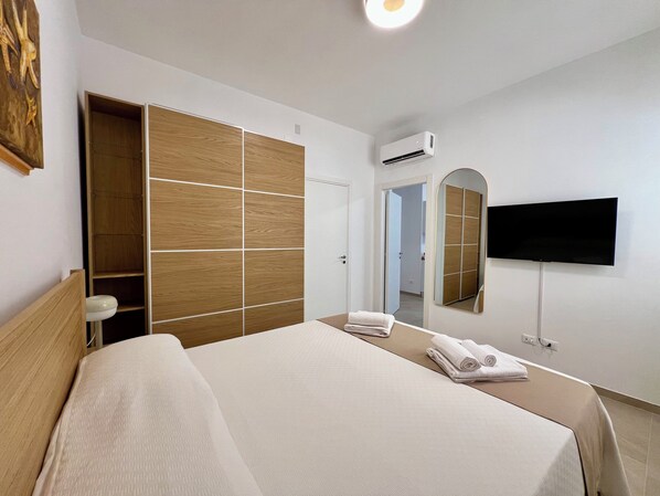 Une chambre d’hôtel équipée d’un lit, d’une armoire, d’un climatiseur, d’une télévision et d’un miroir.