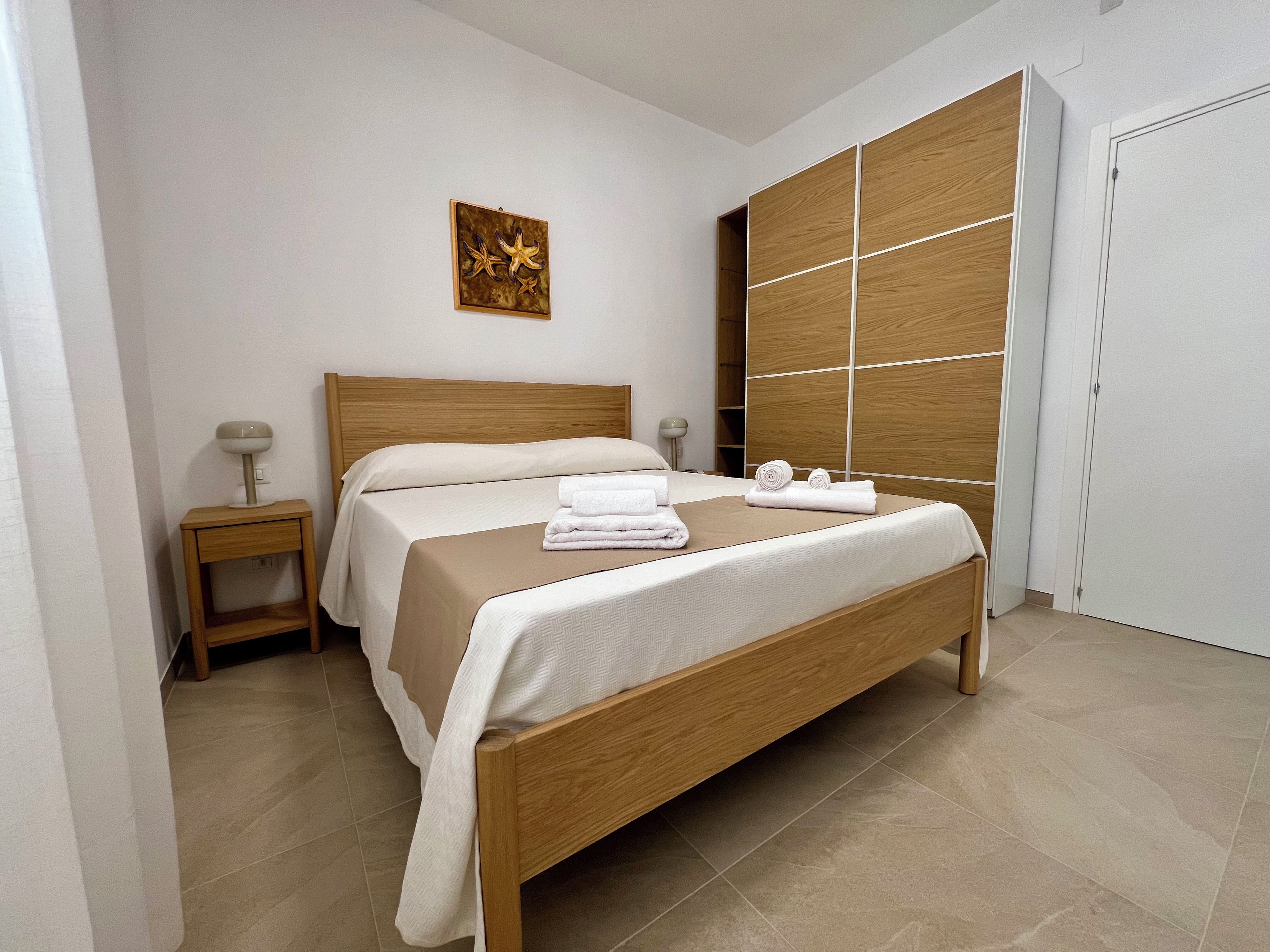 Un lit bien fait, avec une tête de lit en bois, une table de chevet avec une lampe et une grande armoire avec un miroir.