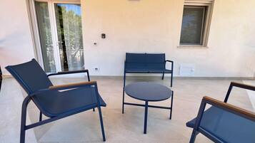 A patio area with a round table and two lounge chairs, a bench, and a sliding glass door.