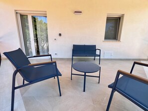 A patio area with a round table and two lounge chairs, a bench, and a sliding glass door. - Villa Favorita: Casa Beige—Between Nature and Mondello (Palermo)