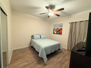 A bedroom with a bed, a ceiling fan, a painting, and a desk with a keyboard. - Perfect Getaway Duplex for Short or Long Term Stays! (Brownsville)