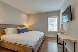 Ein Schlafzimmer mit einem Bett, einem Nachttisch, einer Lampe und einem an der Wand befestigten Fernseher.