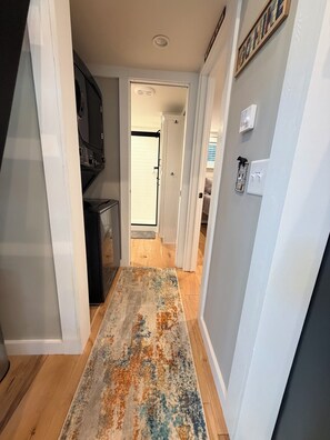 Een gang met een patroonrijk tapijt, een keukenhoek met inbouwapparatuur, en een deur naar een andere kamer.