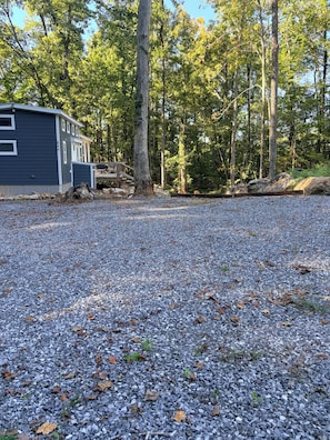 Een grindpad leidt naar een blokhut met een terras, omgeven door bomen.