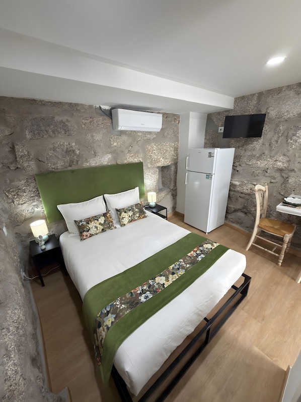 Un dormitorio con cama, mesita de noche, lámpara, televisor, refrigerador y una silla.