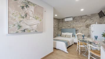 A room with a bed, a table, and a chair. There is a painting on the wall.