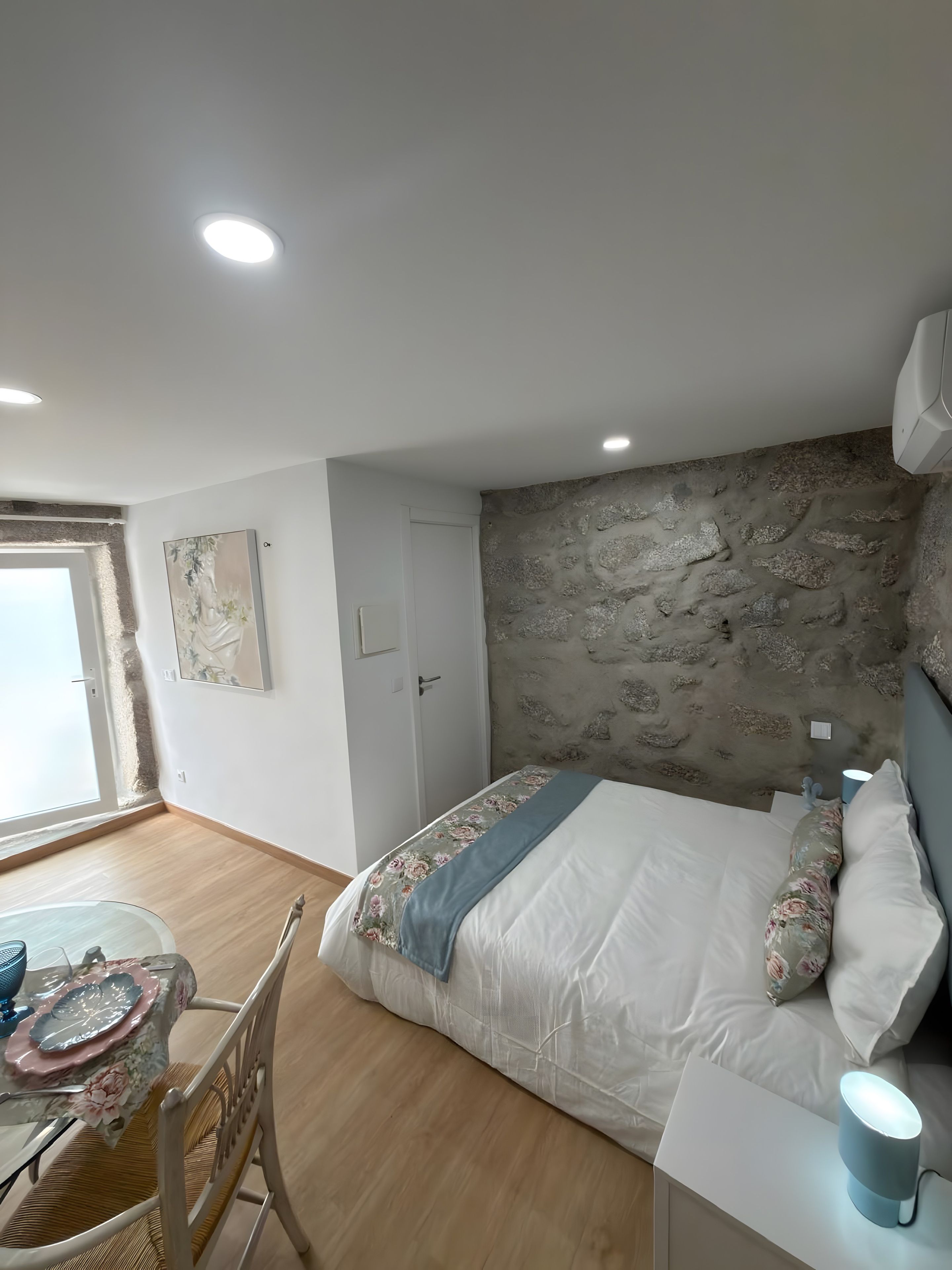 Ein Schlafzimmer mit einem Bett, einem Tisch mit Stühlen, einer Steinwand und einer Tür.