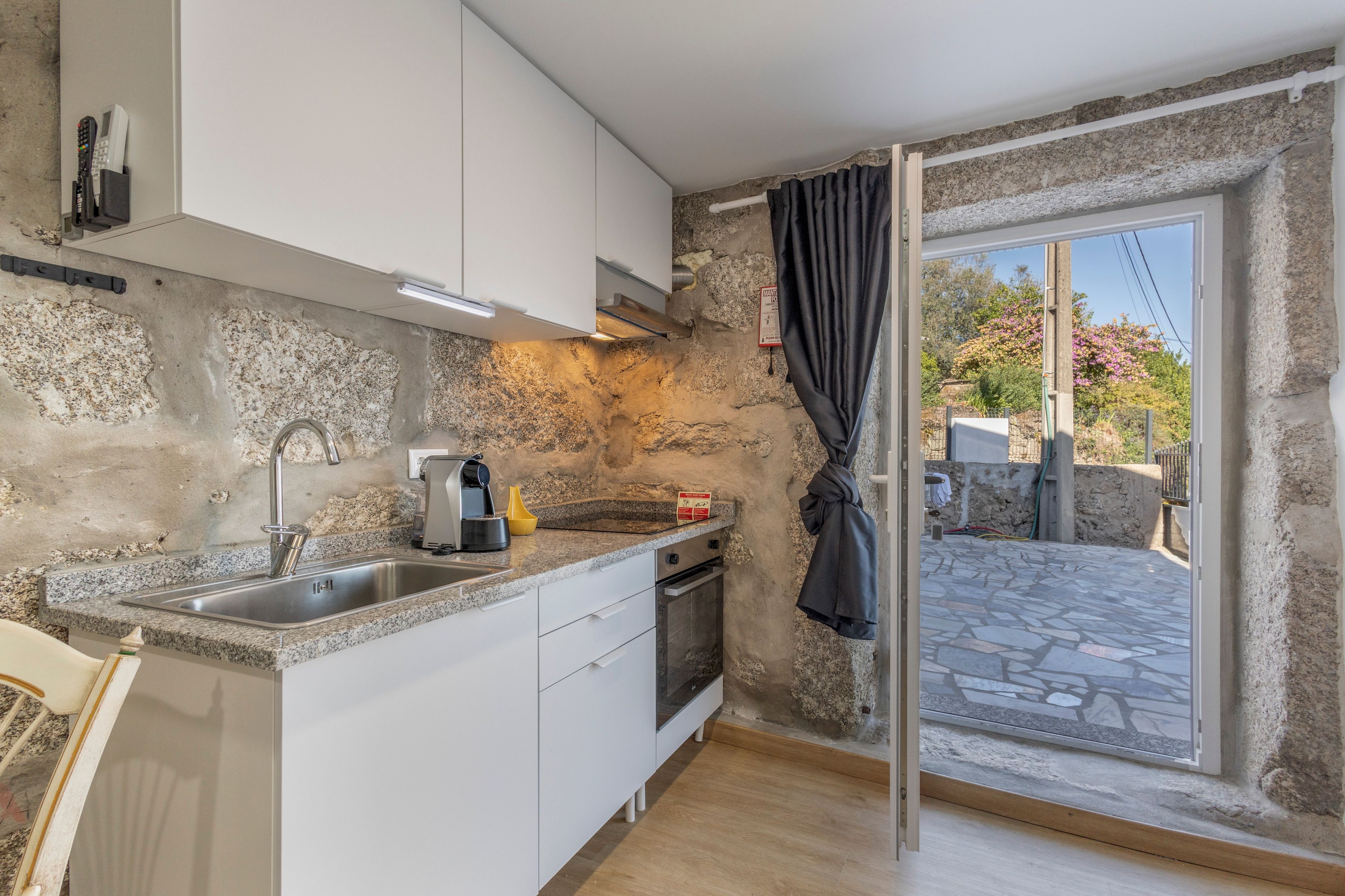 A compact kitchen with a stone wall, a sink, a coffee maker, and a view of the outside.