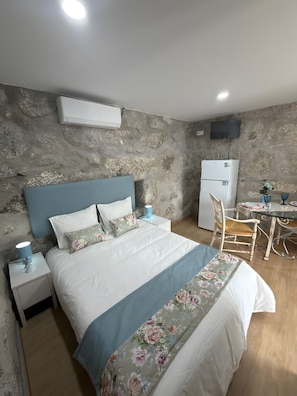 Un dormitorio con pared de piedra, una cama con ropa de cama floral, un escritorio con una silla y un televisor de pantalla plana montado en la pared.
