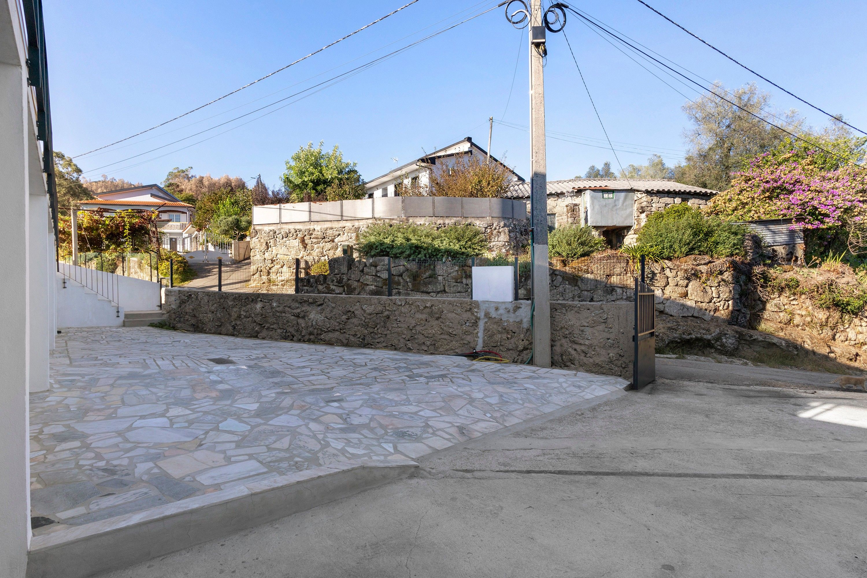 A stone-paved entrance with a metal gate, a stone wall, and a utility pole.