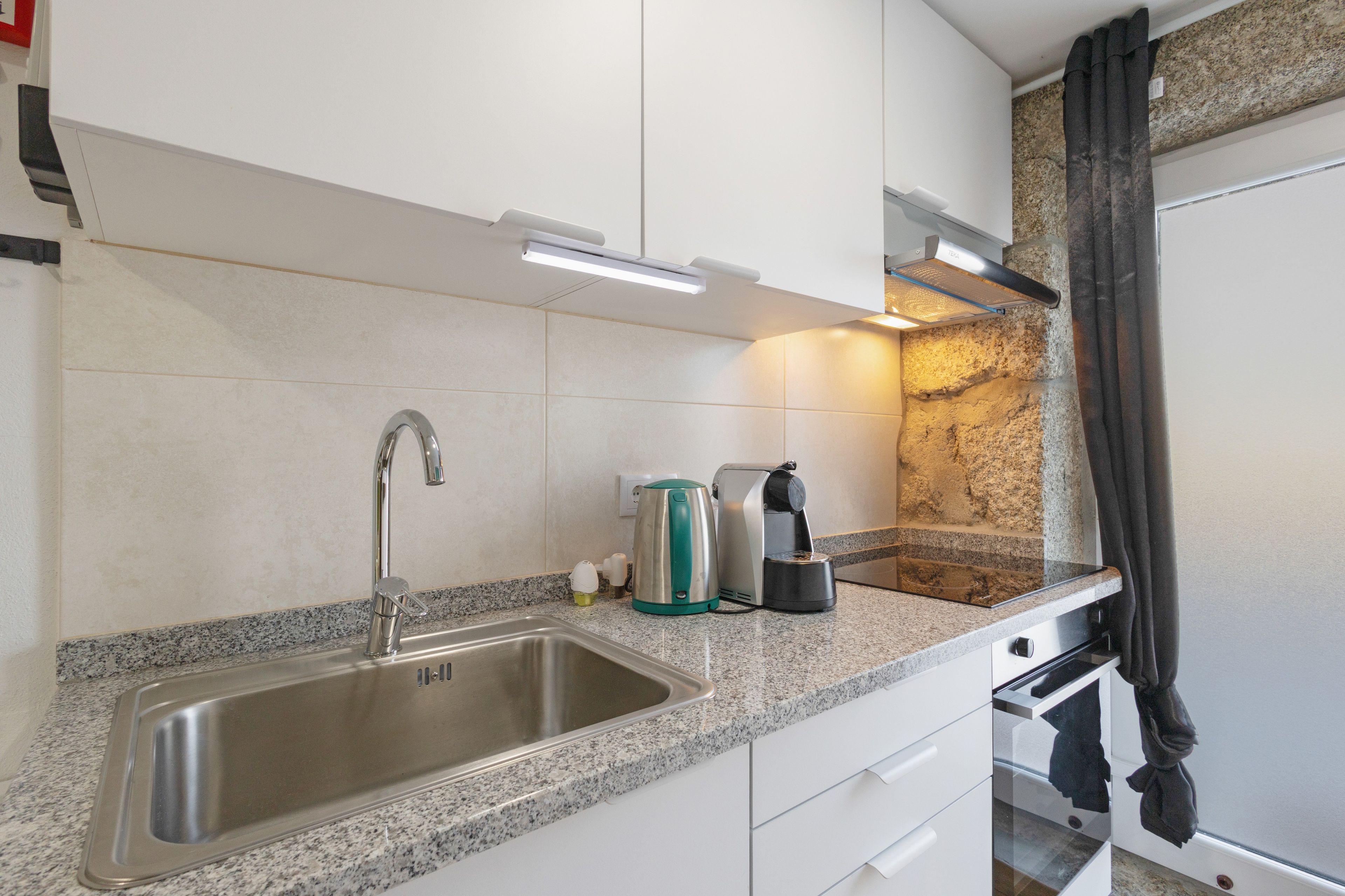 A kitchen with a stainless steel sink, a kettle, and a coffee maker.