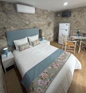 Ein Schlafzimmer mit einem Bett, Nachttischen, einem Sessel, einem Tisch und einem Kühlschrank.