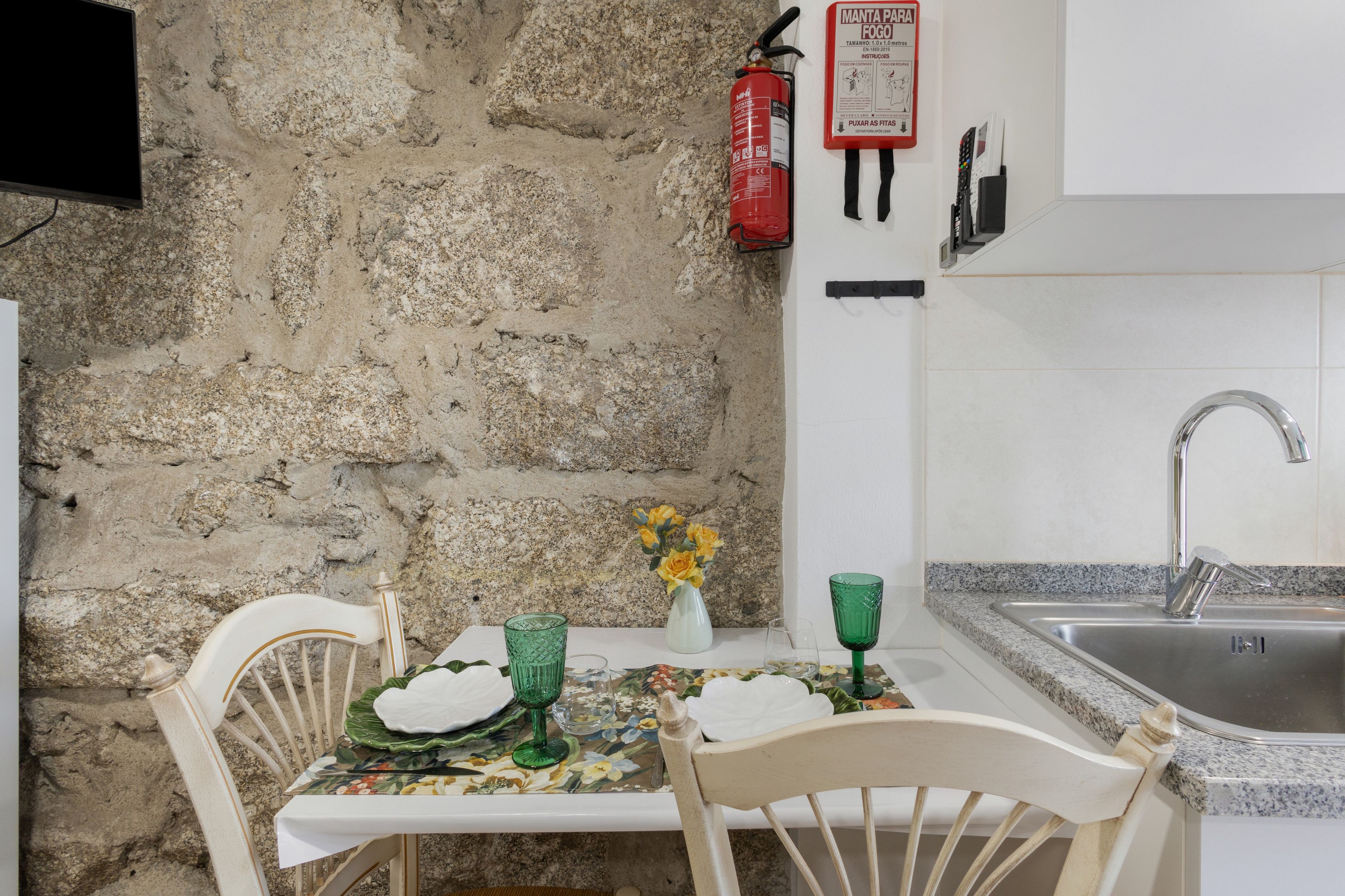 Une cuisine avec un mur en pierre, un extincteur, un évier et une table avec des chaises.