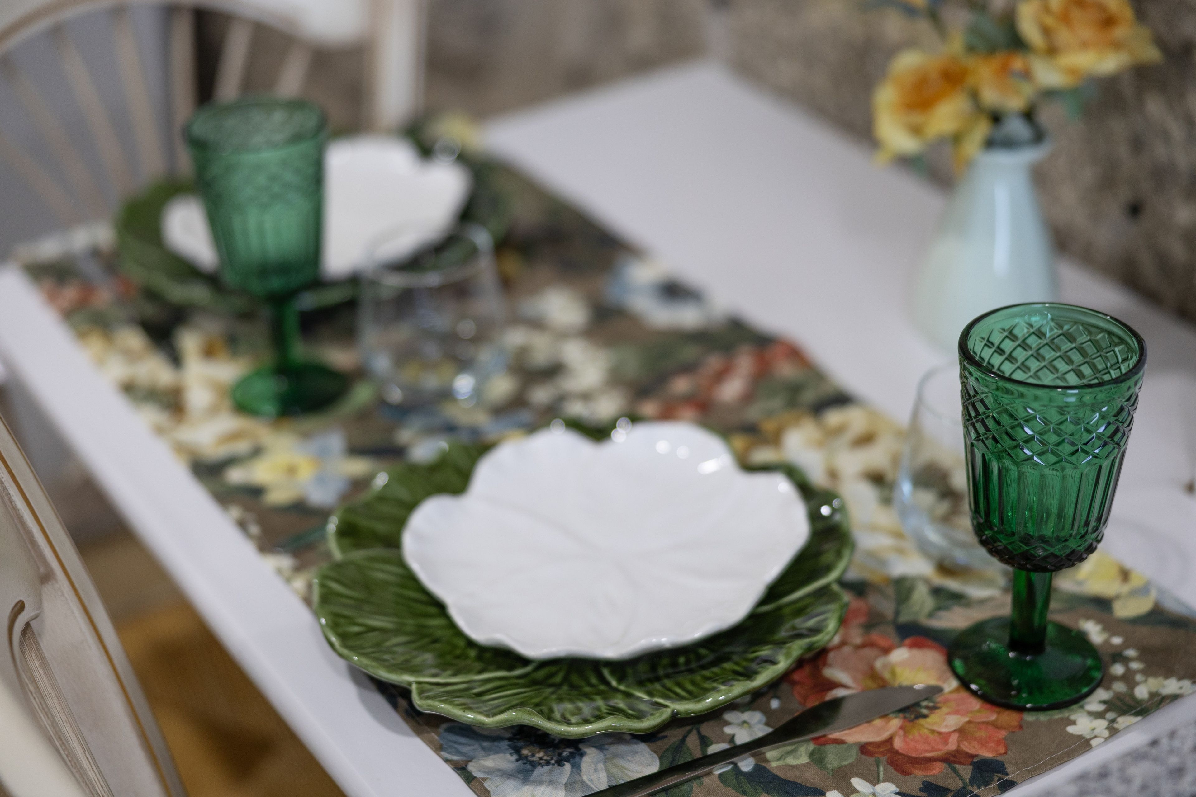 Una mesa dispuesta con cristalería verde y platos blancos sobre un mantel con estampado floral.