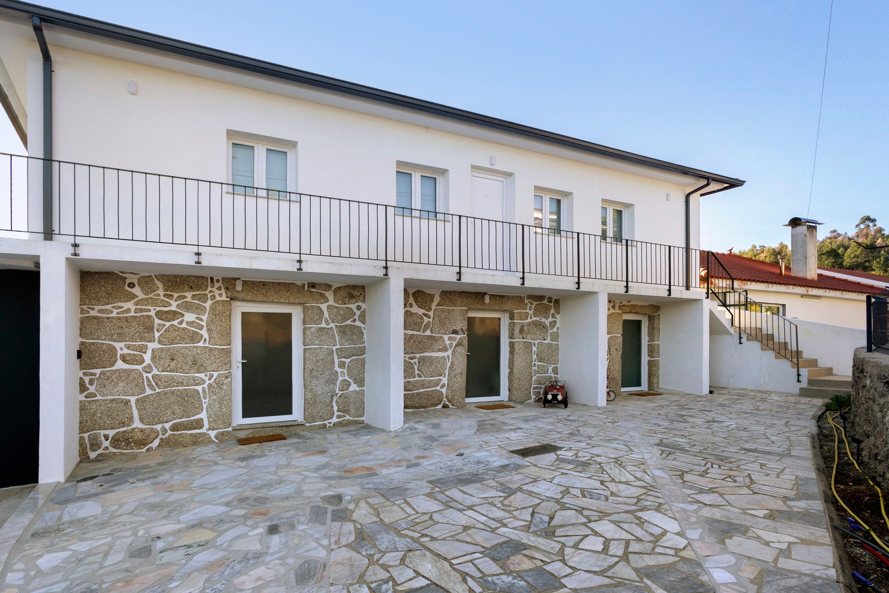 A two-story building with a stone facade, a balcony with a metal railing, and a tiled courtyard.