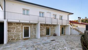 A two-story building with a stone facade, a balcony with a metal railing, and a tiled courtyard.
