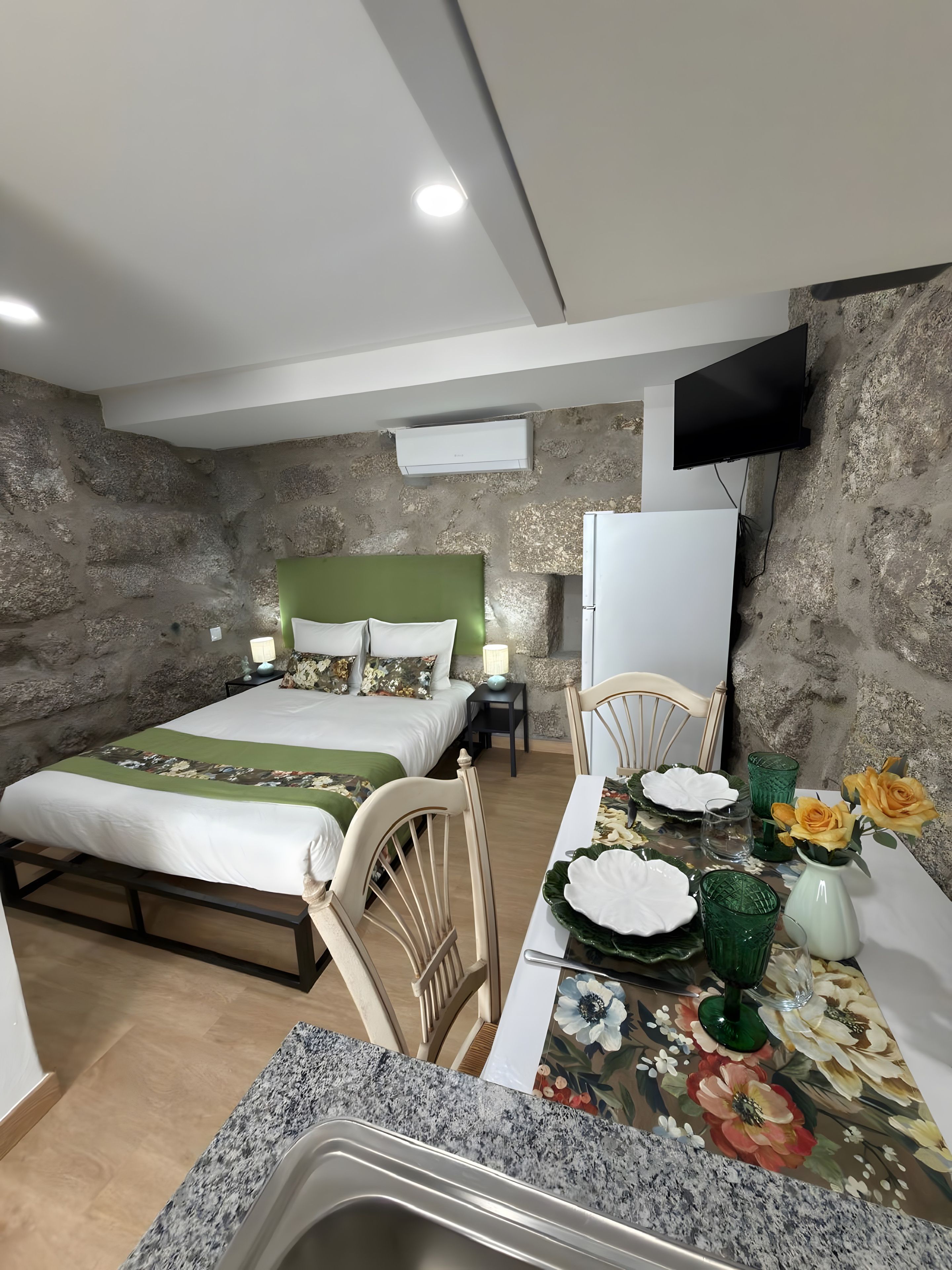A bedroom with a bed, bedside tables, a television, and a dining area with a table set for two.