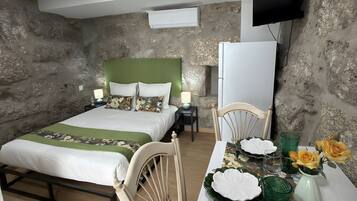 A bedroom with a bed, bedside tables, a television, and a dining area with a table set for two.