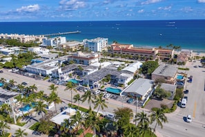 An aerial view of a coastal hotel area with multiple buildings, a swimming pool, and a pier extending into the ocean. - Comfy 1 Bed 1 Bath Apt Minutes to the Beach, Pool (Lauderdale-by-the-Sea)