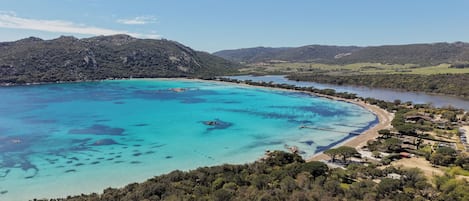 Eine Küstenlandschaft mit klarem türkisblauem Meer, einem Sandstrand und einem bewaldeten Hügel.