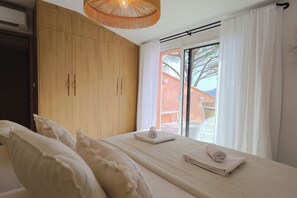 A bedroom with a bed, wooden wardrobe, and a window with curtains. - U Mulinu | Villa with Ocean Views | Panorama Santa Giulia (Porto-Vecchio)