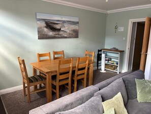 A dining area with a wooden table and chairs, a gray sofa, and a wall-mounted picture of a boat. - Spacious and comfortable town house close to the beach and town! (Bournemouth)