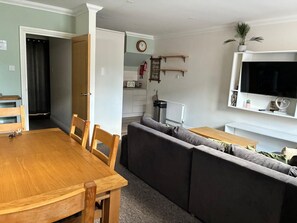 A living room with a wooden dining table, grey sofa, and a TV mounted on the wall. - Spacious and comfortable town house close to the beach and town! (Bournemouth)