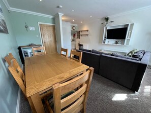A dining area with a wooden table and chairs, a living room with a sofa, and a kitchen in the background. - Spacious and comfortable town house close to the beach and town! (Bournemouth)