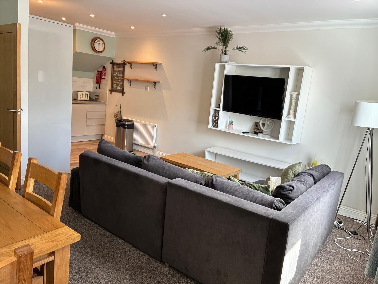 Un salon avec un canapé gris, une table basse en bois et un téléviseur fixé au mur.