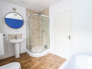 A bathroom with a glass-enclosed shower, a white sink, and a round mirror. - Flat 4 Greenfields (Barmouth)