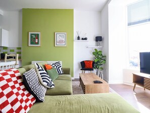 A modern living room with a green sofa, a wooden coffee table, and a TV stand. - Flat 1 Greenfields (Barmouth)