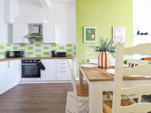 A modern kitchen with white cabinets, a black oven, and a green-tiled backsplash. - Flat 1 Greenfields (Barmouth)