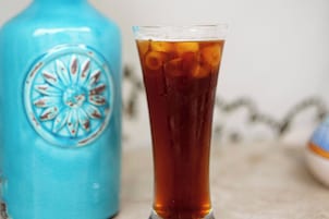 Un vaso transparente de té helado junto a una botella azul con un emblema decorativo.