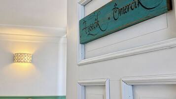 A teal sign with 'Aysceir' and 'Omarik' written on it, mounted on a white wall with a light fixture above.