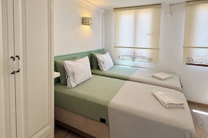 Habitación de hotel con dos camas, una ventana con cortinas, una lámpara de pared y suelo de madera.