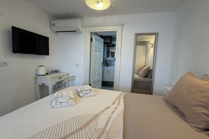 Habitación de hotel con cama, escritorio con tetera, televisión de pantalla plana y aire acondicionado.